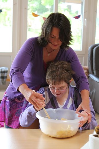 Eine Mitarbeiterin hilft einer Frau mit Behinderung beim kochen