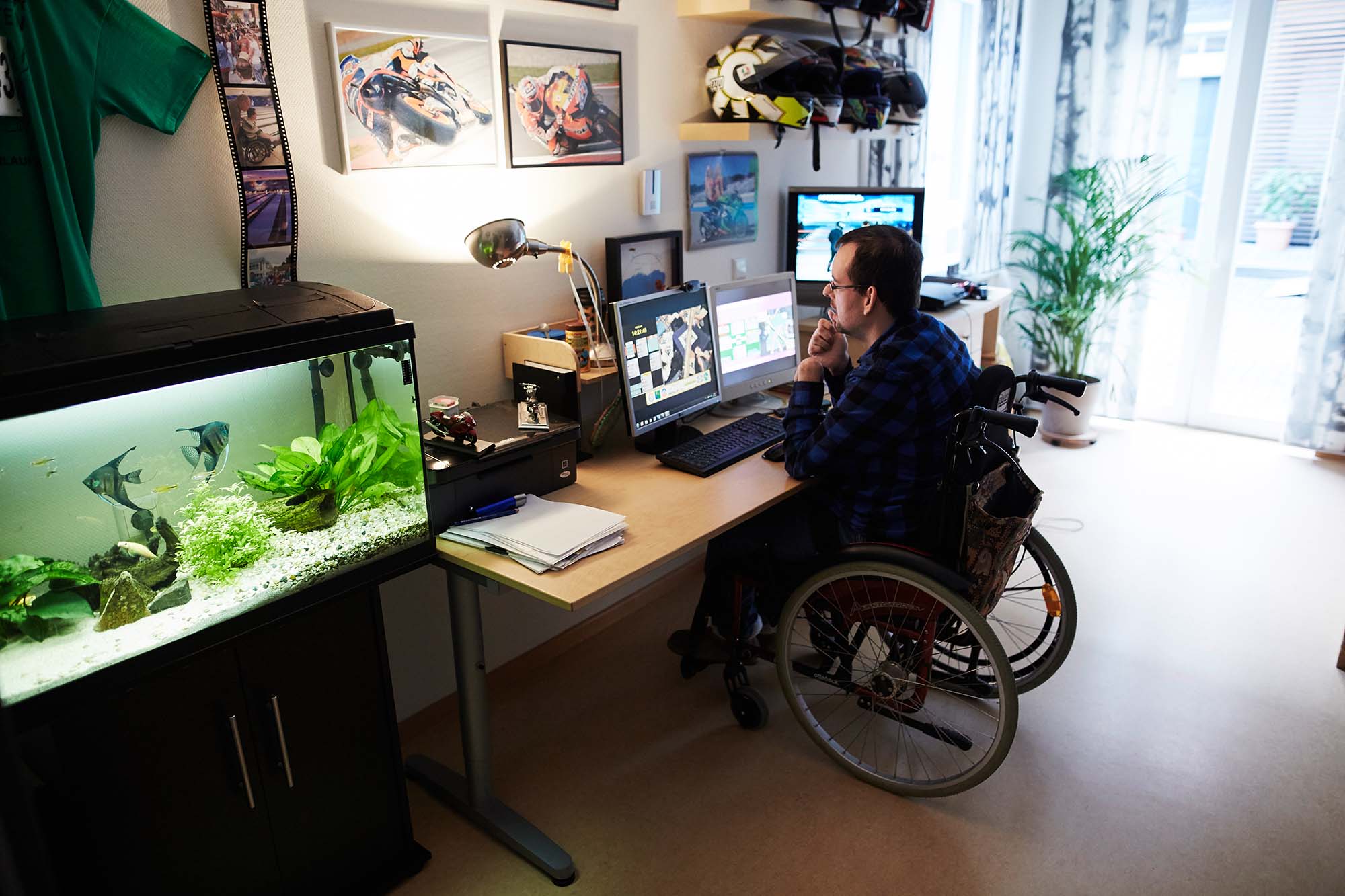 Ein Mann im rollstuhl sitzt in seinem Zimmer am Computer.