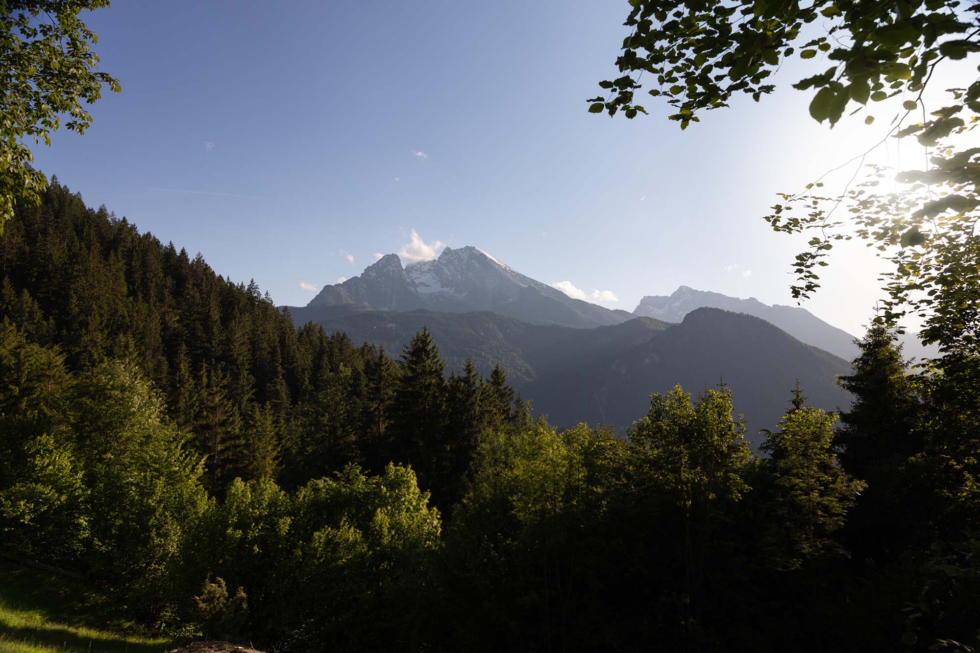 Ein Landschaftsbild aus Berchtesgaden: Zu sehen ist der Watzmann, grüne Wälder und ein sommerlicher Himmel.