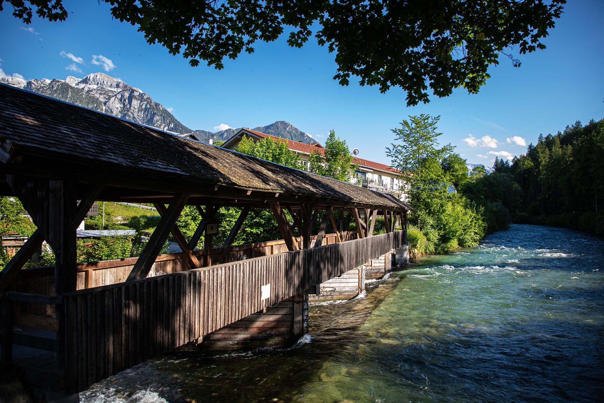 Der Holzsteg über den Bach, der am Wohnhaus vorbei fließt. im Hintergrund sind die Berchtesgadener Berge zu sehen. 